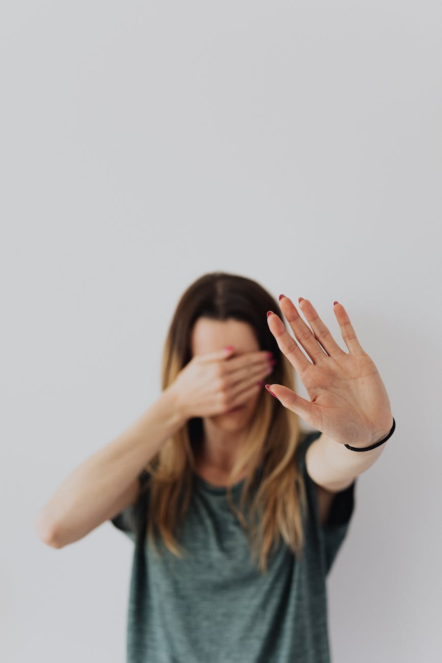 a woman covering her face with hand and showing a stop gesture