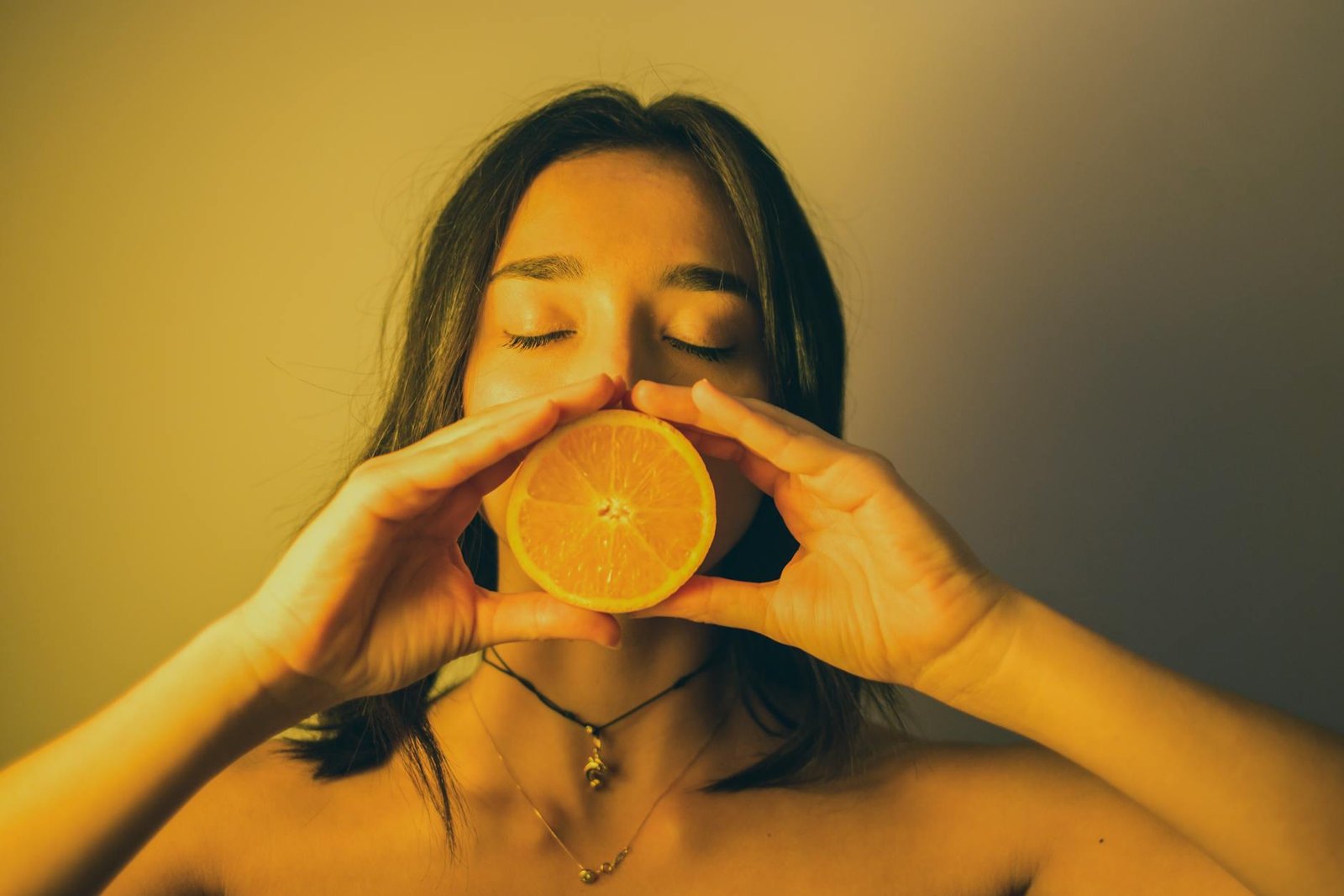 attractive woman with eyes closed holding orange slice against lips