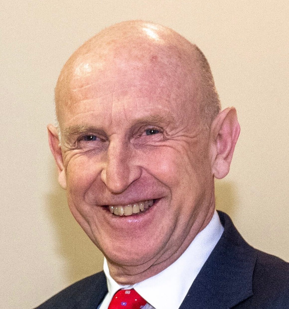 Smiling older man in a dark suit and red tie, facing the camera in a head-and-shoulders portrait.